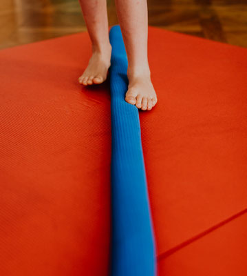 Kinderfüße stehen auf blauer Balance-Rolle auf rotem Trampolin