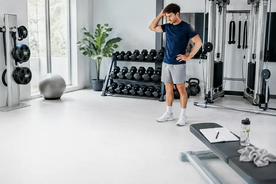 Mann im Home-Gym mit besorgtem Gesichtsausdruck und Trainingsgeräten im Hintergrund