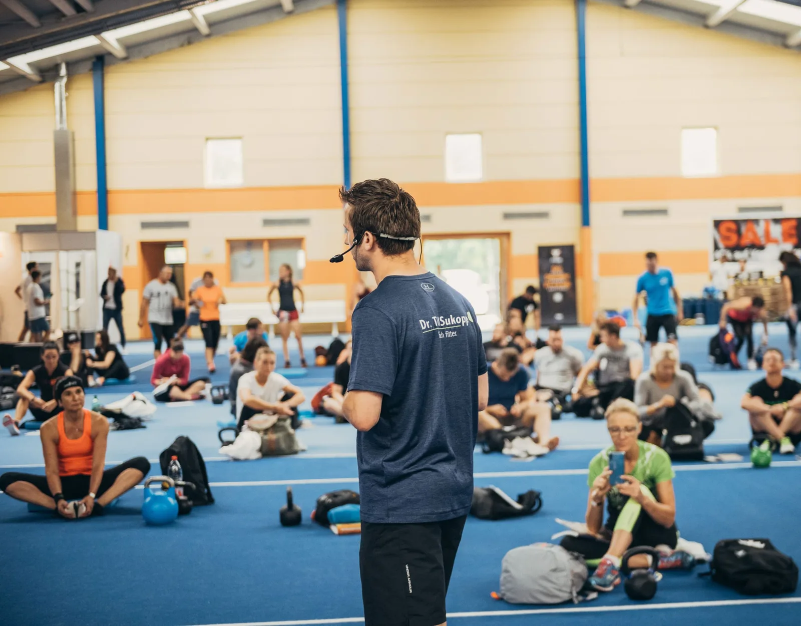 Zurück zur Kraft – Videokurs für Beweglichkeit von Till Sukopp 10 Till Sukopp präsentiert vor Gruppenkurs in moderner Sporthalle mit Matten und Kettlebells