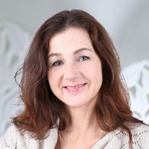 Porträt von Nika Herzog mit grauem Haar, Brille, rosa Hemd vor unscharfem Außenhintergrund