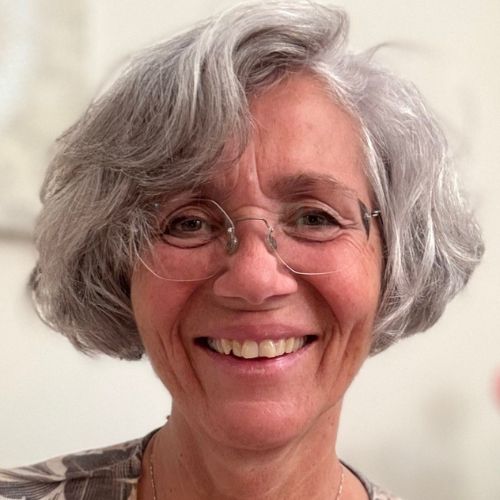 Porträt von Simone Anliker mit grauem Haar und Brille, lächelnd vor neutralem Hintergrund