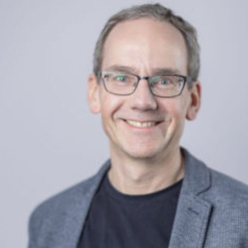 Porträt von Matthias Herzog mit Brille vor grauem Hintergrund