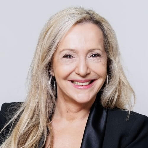 Porträt von Susan Froitzheim, blonde Frau mit langem Haar und schwarzer Jacke vor grauem Hintergrund