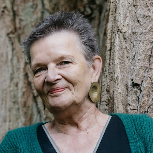Porträt von Claudia Cardinal mit grauem Haar, Ohrring, schwarzem Jacket vor grünem Hintergrund